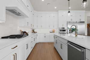 Kitchen featuring white cabinets, stainless steel appliances, custom range hood, light stone counters, and recessed lighting