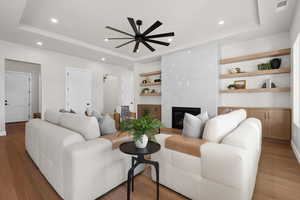 Living area featuring built in features, a premium fireplace, wood finished floors, recessed lighting, and a raised ceiling
