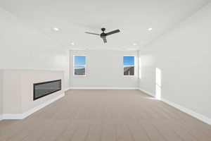 Unfurnished living room featuring light colored carpet, a glass covered fireplace, recessed lighting, and a ceiling fan