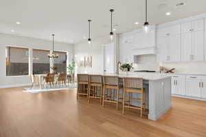 Kitchen featuring pendant lighting, white cabinets, a breakfast bar area, light wood finished floors, and a kitchen island with sink