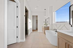 Bathroom featuring a freestanding tub, two vanities, a shower stall, a walk in closet, and recessed lighting