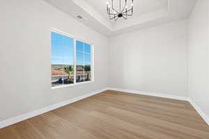 Spare room with a tray ceiling, a chandelier, and light wood finished floors
