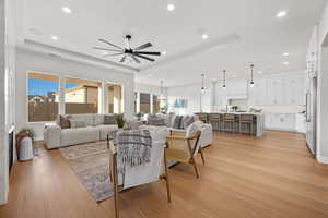 Living room featuring light wood finished floors, a raised ceiling, recessed lighting, and a ceiling fan