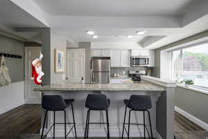 Kitchen with white cabinets, appliances with stainless steel finishes, light stone counters, decorative backsplash, and a breakfast bar area
