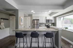 Kitchen featuring appliances with stainless steel finishes, white cabinets, a kitchen bar, light stone countertops, and tasteful backsplash
