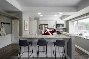 Kitchen featuring stainless steel appliances, white cabinetry, decorative backsplash, a kitchen bar, and light stone counters