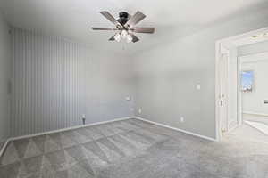Carpeted empty room featuring a ceiling fan and an accent wall