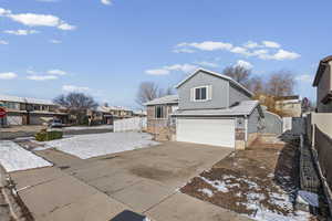 Tri-level home featuring an attached garage, driveway, brick siding, a residential view, and a gate