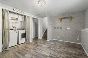 Laundry room with washer and dryer, wood finished floors, a textured ceiling, an accent wall, and brick wall