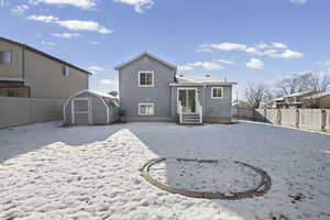 Snow covered house with a shed, a fenced backyard, and entry steps