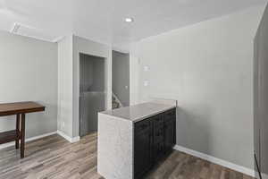 Kitchen featuring dark cabinetry, light stone countertops, a textured ceiling, a peninsula, and light wood finished floors