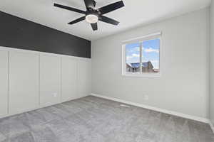 Unfurnished bedroom featuring a decorative wall, wainscoting, light colored carpet, and a ceiling fan