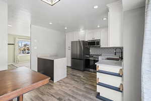 Kitchen with light stone countertops, appliances with stainless steel finishes, white cabinets, a textured ceiling, and tasteful backsplash