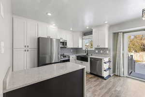 Kitchen featuring light stone counters, appliances with stainless steel finishes, white cabinets, decorative backsplash, and recessed lighting
