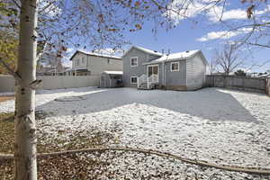 Snow covered house with a fenced backyard, a storage shed, and entry steps