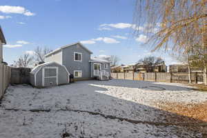 Snow covered rear of property with a storage unit and a fenced backyard