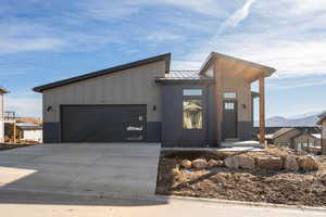 Modern home featuring a standing seam roof, a metal roof, concrete driveway, a garage, and board and batten siding