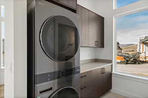 Laundry area with plenty of natural light, cabinet space, and stacked washer and clothes dryer