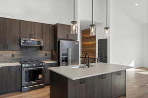 Kitchen featuring high vaulted ceiling, dark brown cabinetry, stainless steel appliances, hanging light fixtures, and modern cabinets