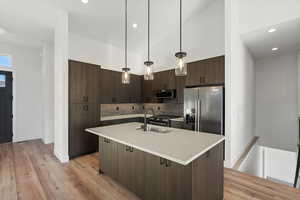 Kitchen with dark brown cabinets, an island with sink, high end appliances, high vaulted ceiling, and decorative light fixtures