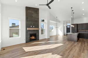 Unfurnished living room featuring high vaulted ceiling, recessed lighting, ceiling fan, a tile fireplace, and light wood-style floors