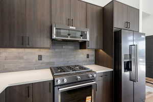 Kitchen featuring modern cabinets, appliances with stainless steel finishes, dark brown cabinets, and tasteful backsplash