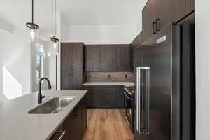 Kitchen featuring modern cabinets, high end fridge, dark brown cabinets, gas stove, and hanging light fixtures