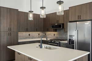 Kitchen with stainless steel appliances, dark brown cabinetry, an island with sink, and decorative light fixtures