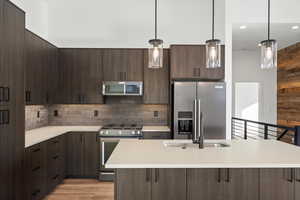 Kitchen featuring decorative light fixtures, stainless steel appliances, dark brown cabinetry, light wood-type flooring, and wood walls