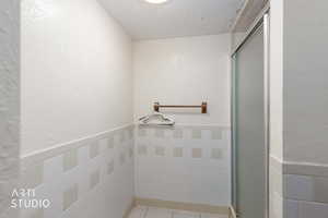 Full bathroom featuring a wainscoted wall, a stall shower, and a textured wall