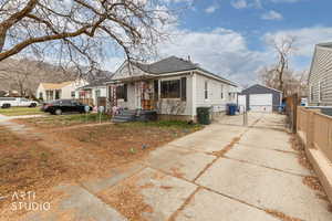 View of front of property with a detached garage, driveway, an outdoor structure, and a gate