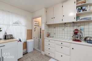 Kitchen with white cabinetry, open shelves, tile countertops, wainscoting, and tasteful backsplash