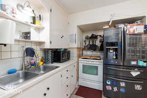 Kitchen with stainless steel fridge, electric stove, white cabinets, decorative backsplash, and ornamental molding