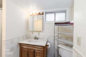 Half bathroom featuring wainscoting, vanity, a textured wall, and tile walls