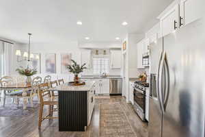 Kitchen featuring appliances with stainless steel finishes, white cabinetry, hanging light fixtures, a center island, and a kitchen bar