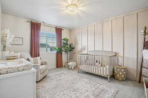 Bedroom featuring a crib, light carpet, a decorative wall, and a chandelier