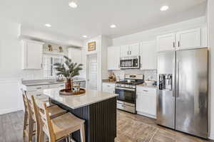 Kitchen featuring stainless steel appliances, white cabinets, light stone countertops, backsplash, and a center island