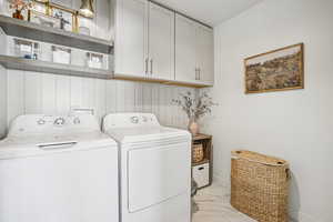 Washroom featuring washing machine and dryer, light marble finish floors, and cabinet space