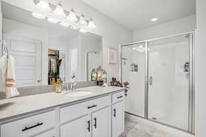 Bathroom with vanity, a spacious closet, a shower stall, and light marble finish flooring