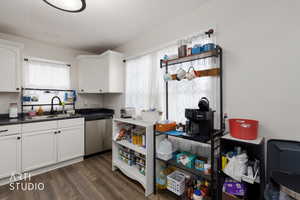 Kitchen featuring dark countertops, white cabinetry, dishwasher, dark wood finished floors, and healthy amount of natural light
