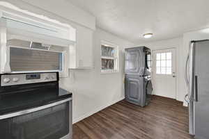 Washroom with dark wood finished floors, stacked washer / dryer, and a textured ceiling