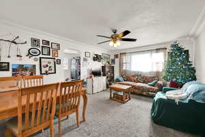 Carpeted living area with ornamental molding, arched walkways, ceiling fan, and a textured ceiling