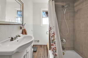 Bathroom with a wainscoted wall, tile walls, vanity, shower / tub combo with curtain, and dark wood-style flooring