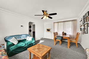 Living room with ornamental molding, arched walkways, carpet flooring, a textured ceiling, and ceiling fan