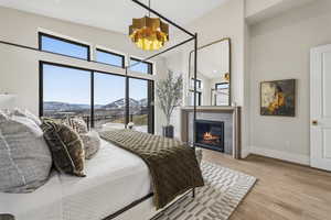 Bedroom featuring wood finished floors, a mountain view, a glass covered fireplace, a chandelier, and access to exterior