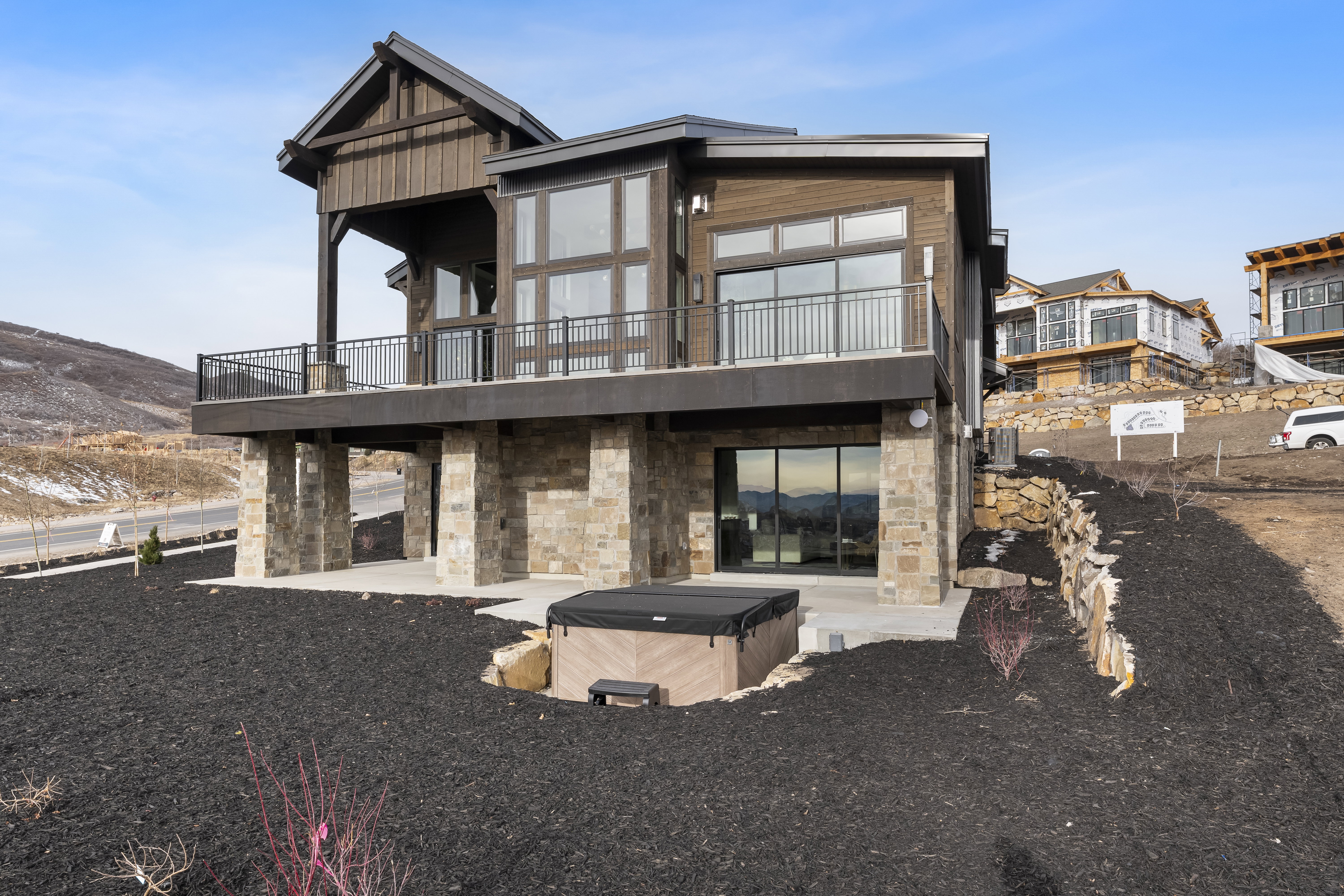Rear view of property with stone siding, a hot tub, a balcony, and a patio area