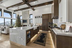 Kitchen featuring dark brown cabinets, light stone countertops, glass insert cabinets, beam ceiling, and a high ceiling