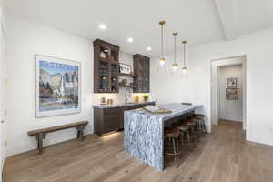 Indoor wet bar featuring dark brown cabinetry, open shelves, decorative light fixtures, light stone countertops, and light wood finished floors