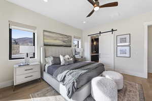 Bedroom featuring a barn door, light wood-style floors, ensuite bath, multiple windows, and recessed lighting