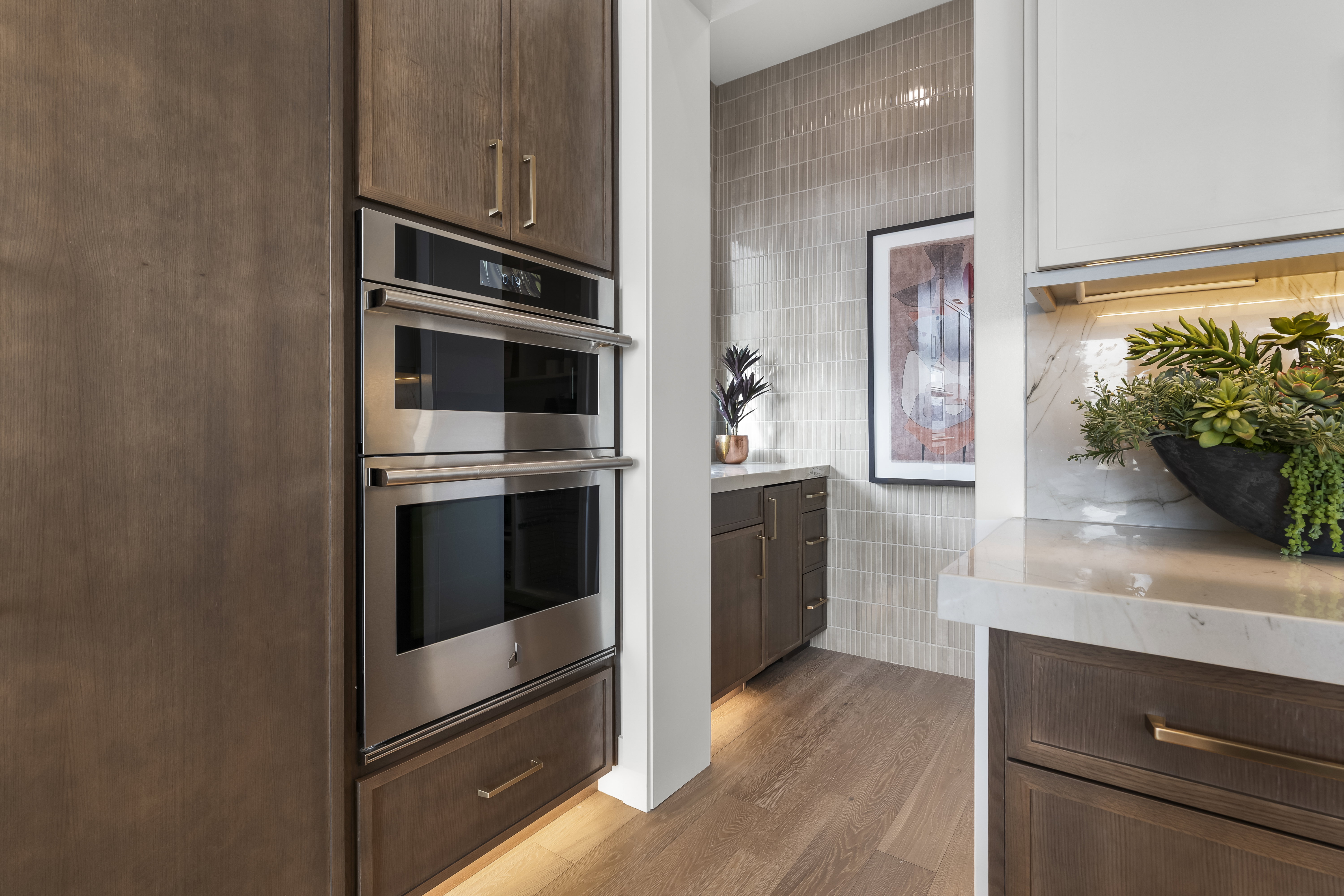 Kitchen featuring tile walls, double oven, light wood-type flooring, and light stone countertops